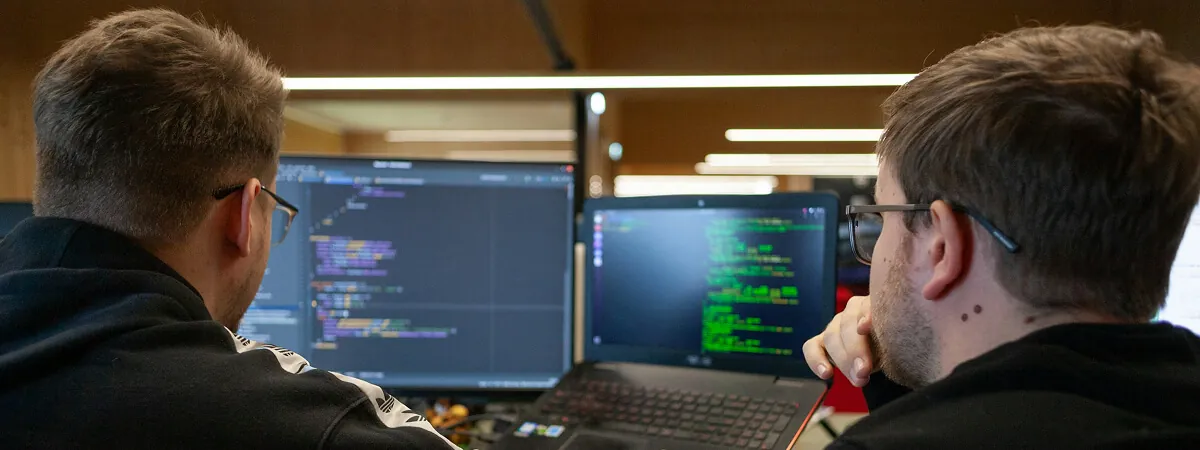 Two developers reviewing code on dual monitors together in an office