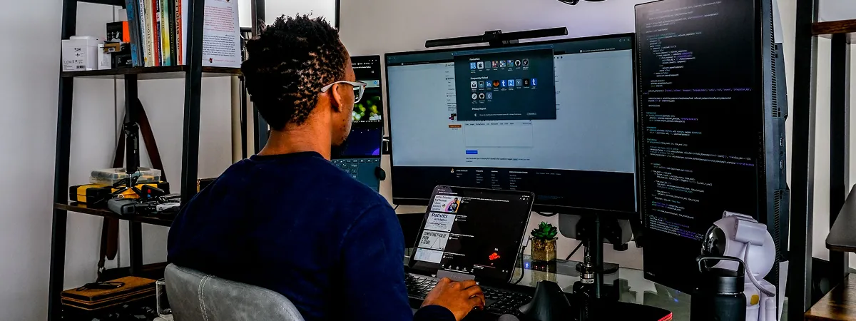 Developer at a multi-monitor home workstation with a code editor and browser open